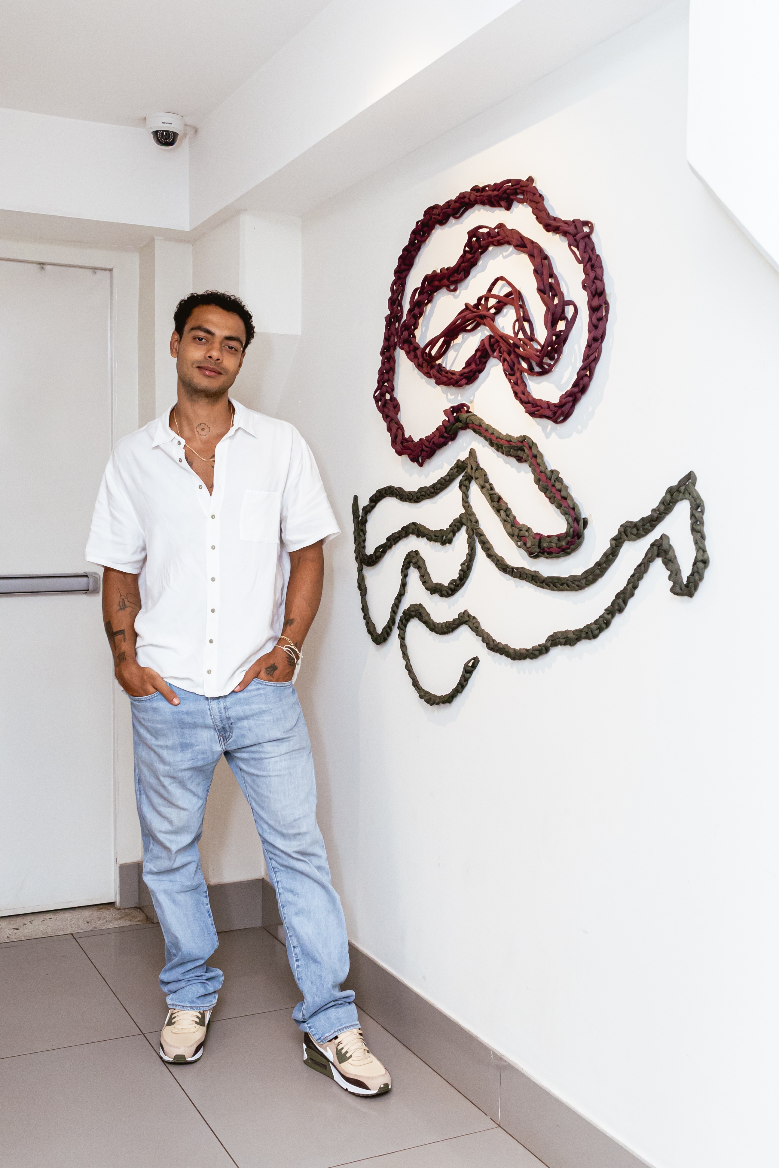 Instalação escultural Correntes com cordas trançadas em burgundy e verde oliva formando padrões orgânicos fluidos na parede