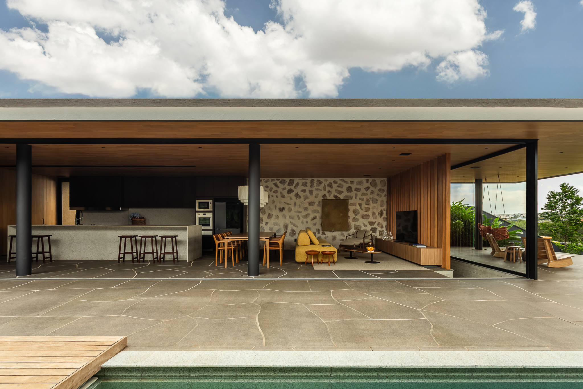 Casa Funchal - Vista diurna externa do pavilhão completo com piscina, deck de madeira, teto ripado e integração total entre interior e exterior