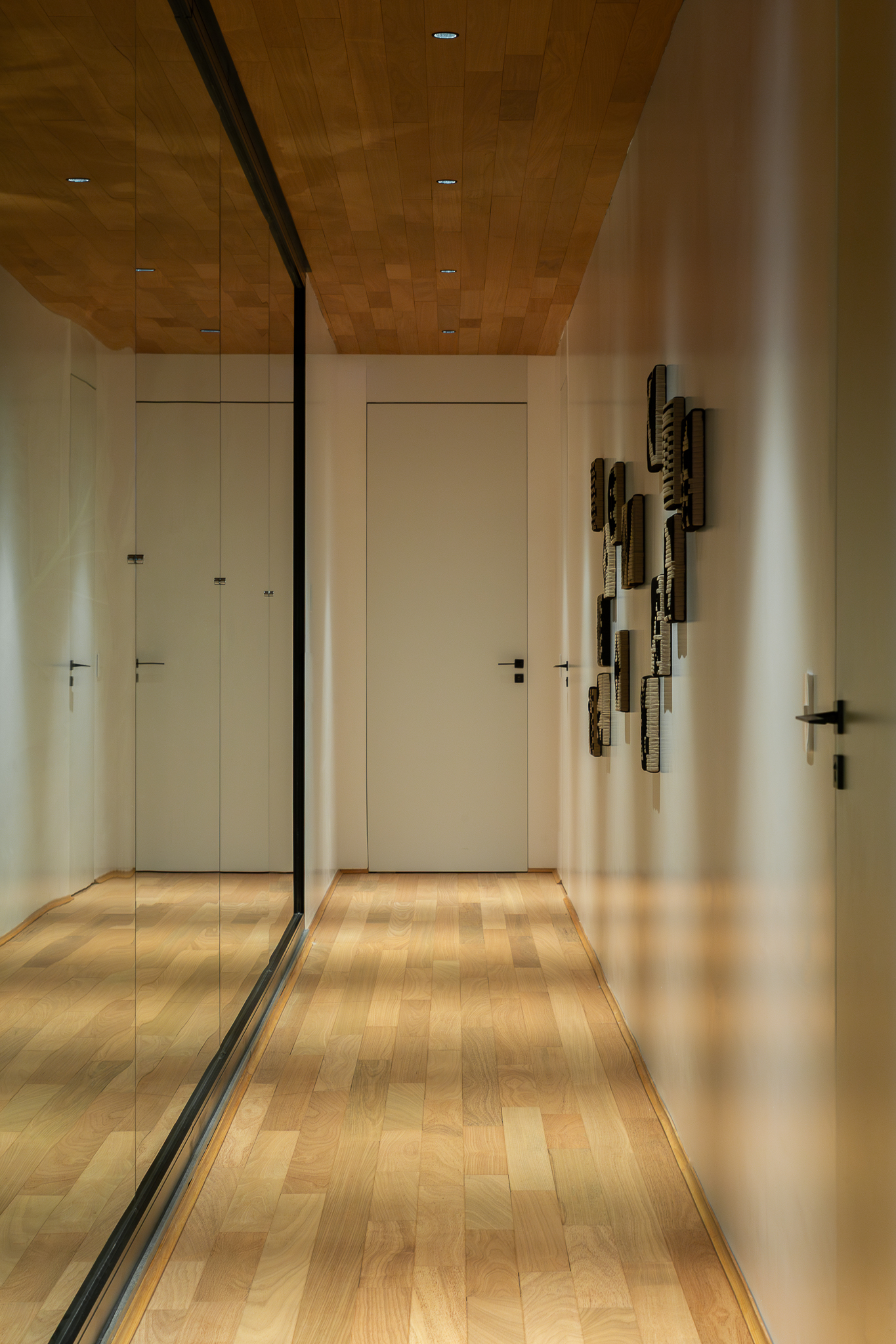 Casa Funchal - Corredor minimalista com teto de madeira, piso claro, espelho de corpo inteiro e obras têxteis verticais na parede