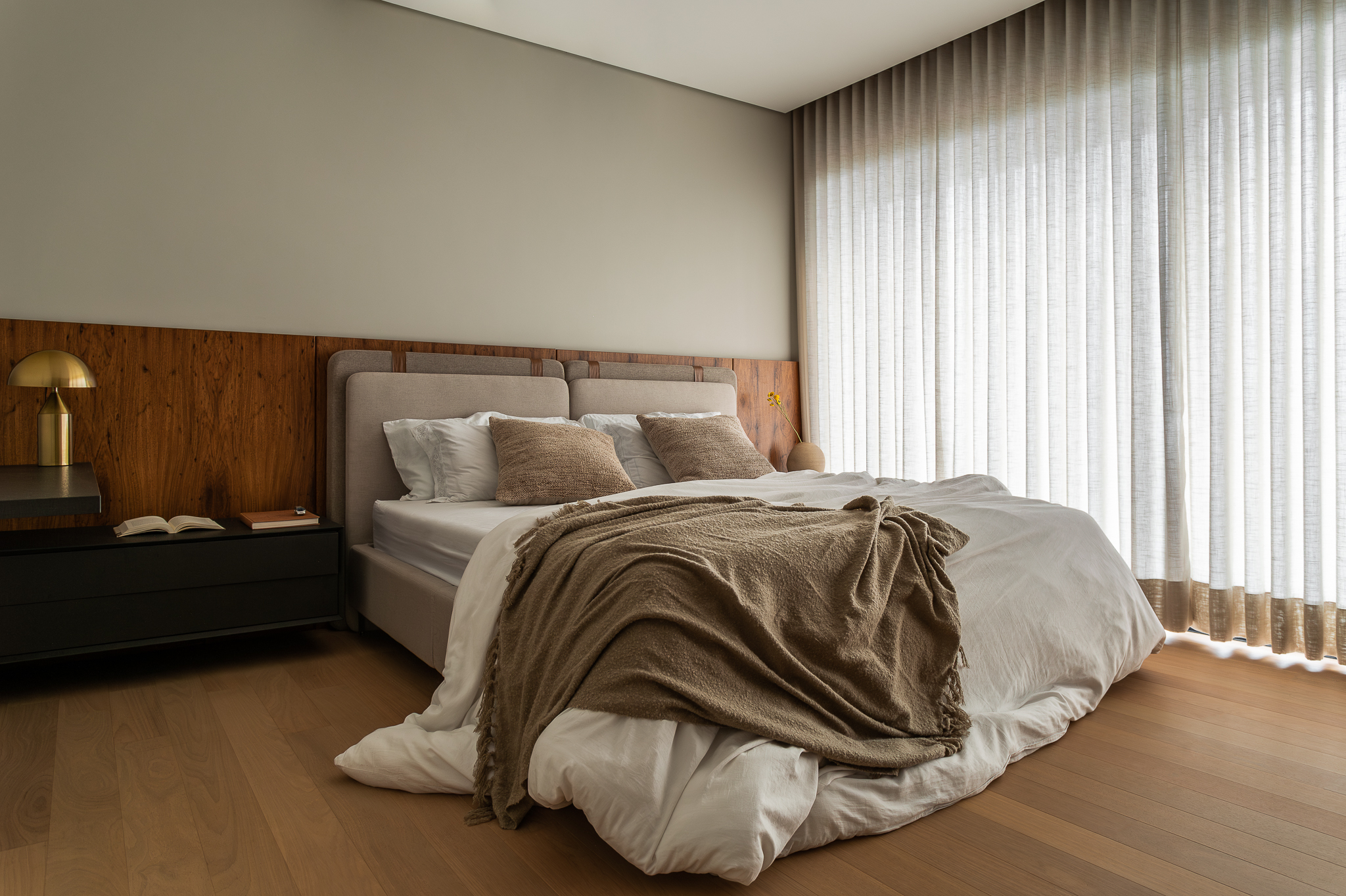 Casa Bosque - Quarto com painel de madeira, cama com roupa de cama bege e cortinas brancas translúcidas